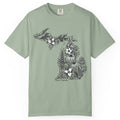 A sage green short-sleeve crewneck t-shirt featuring a black and white graphic of the state of Michigan filled with floral and botanical illustrations, with 'Chaos Caravan' printed below the map.