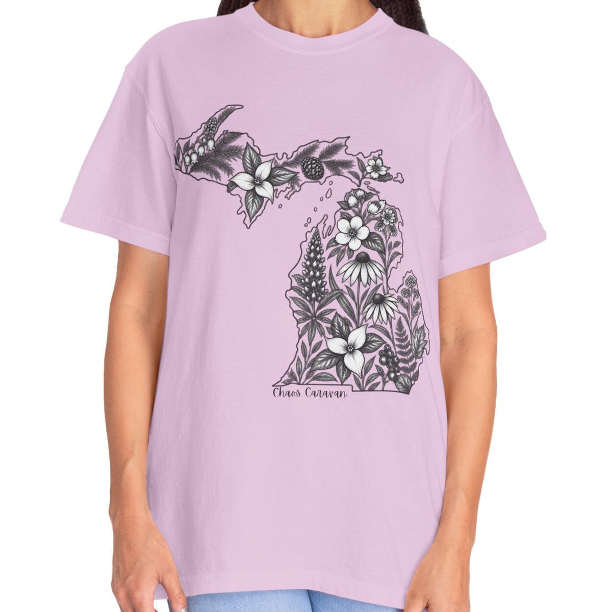 A woman modeling a light purple short-sleeve t-shirt with a black and white floral graphic of the state of Michigan and the text 'Chaos Caravan' on the front, paired with light blue jeans against a plain white background.