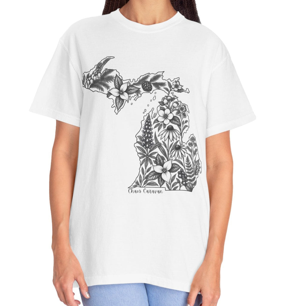 A woman modeling a white short-sleeve crewneck t-shirt with a black graphic of the state of Michigan filled with floral patterns and the text 'Chaos Caravan' below it, paired with light blue jeans against a plain white background.