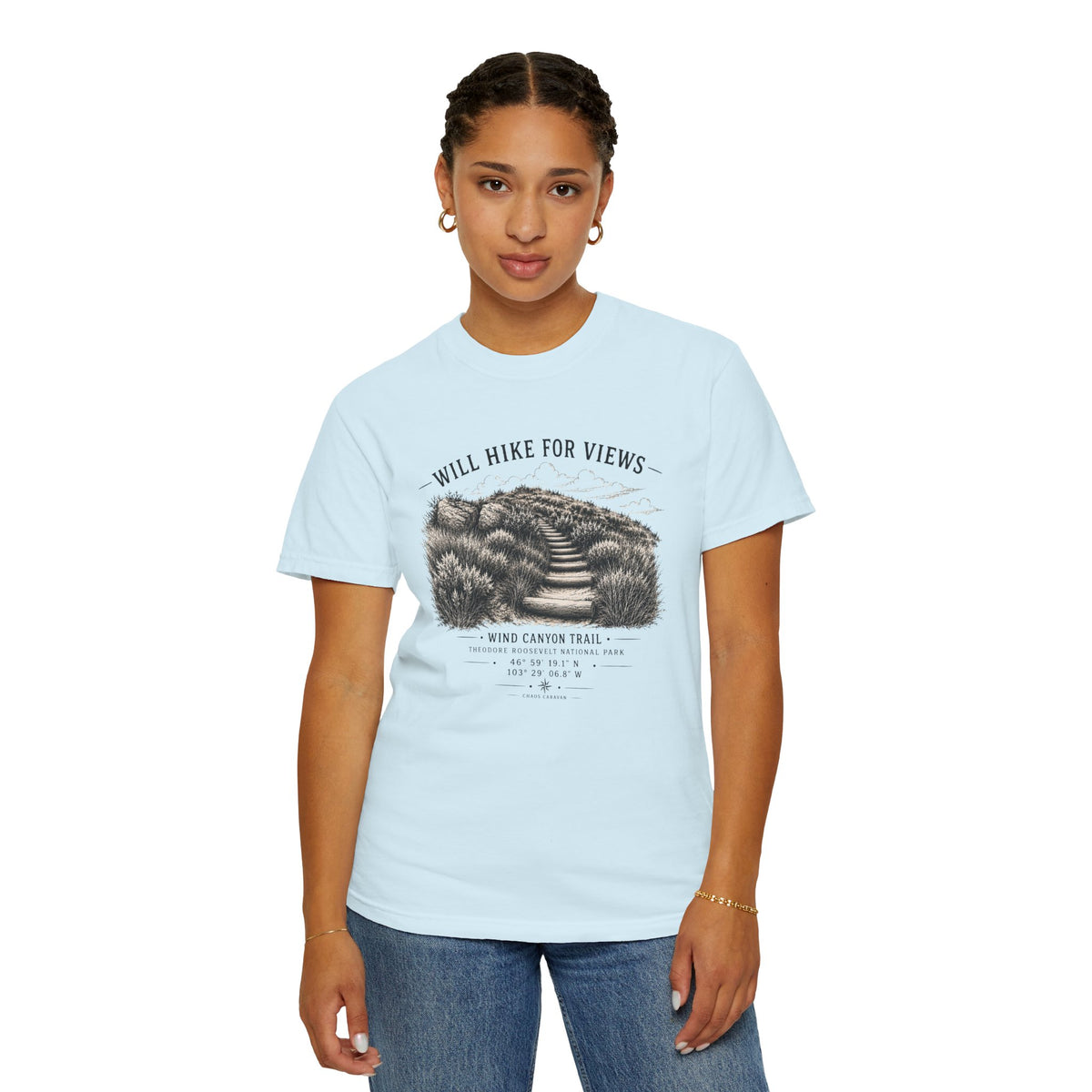 A woman modeling a light blue crewneck t-shirt with a black and white graphic print on the front that reads 'WILL HIKE FOR VIEWS' and 'WIND CANYON TRAIL'.