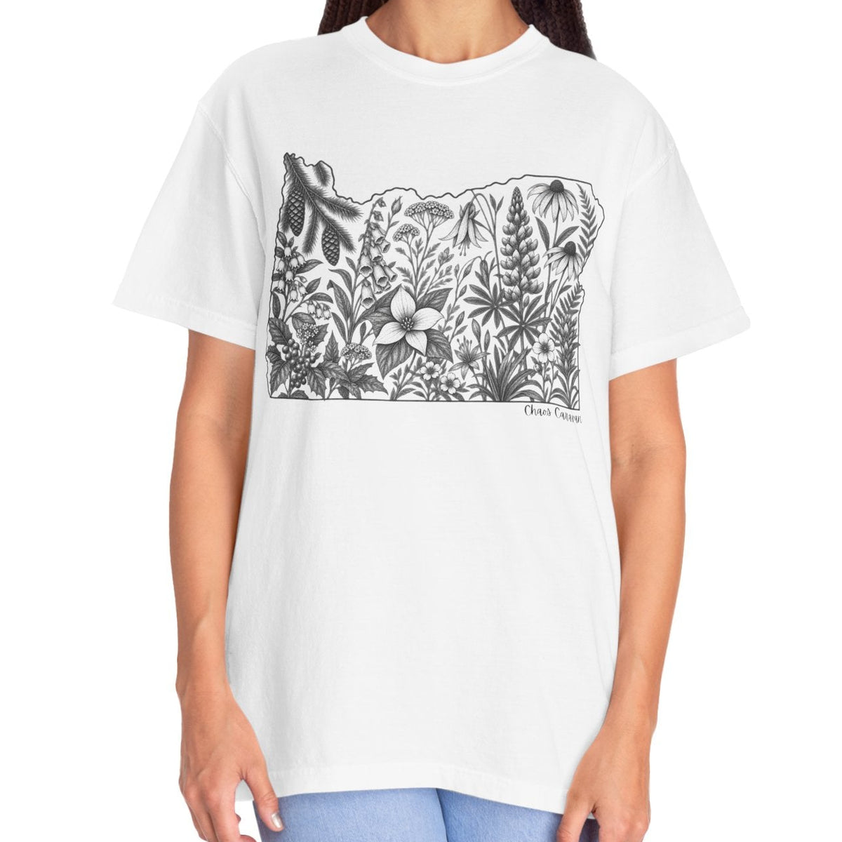 A woman modeling a white short-sleeve crewneck t-shirt with a black line art graphic of a the state of Oregon surrounded by wildflowers, set against a plain white background.