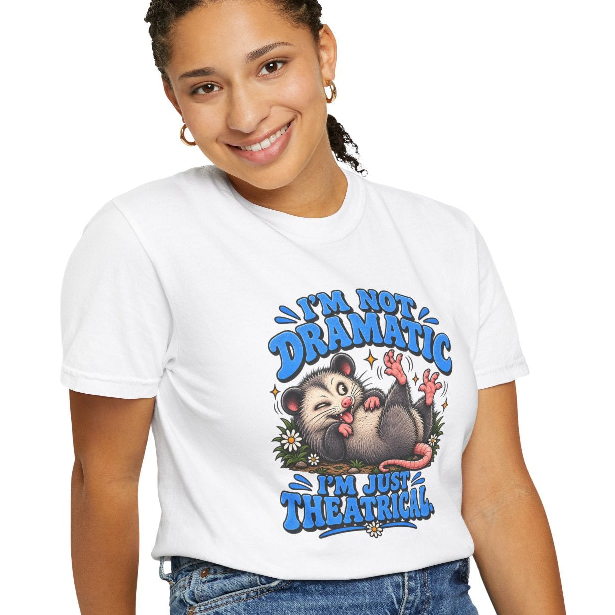 A woman wearing a white graphic t-shirt with a cartoon opossum design and the text 'I'm Not Dramatic I'm Just Theatrical”, paired with blue jeans, posing against a solid white background.
