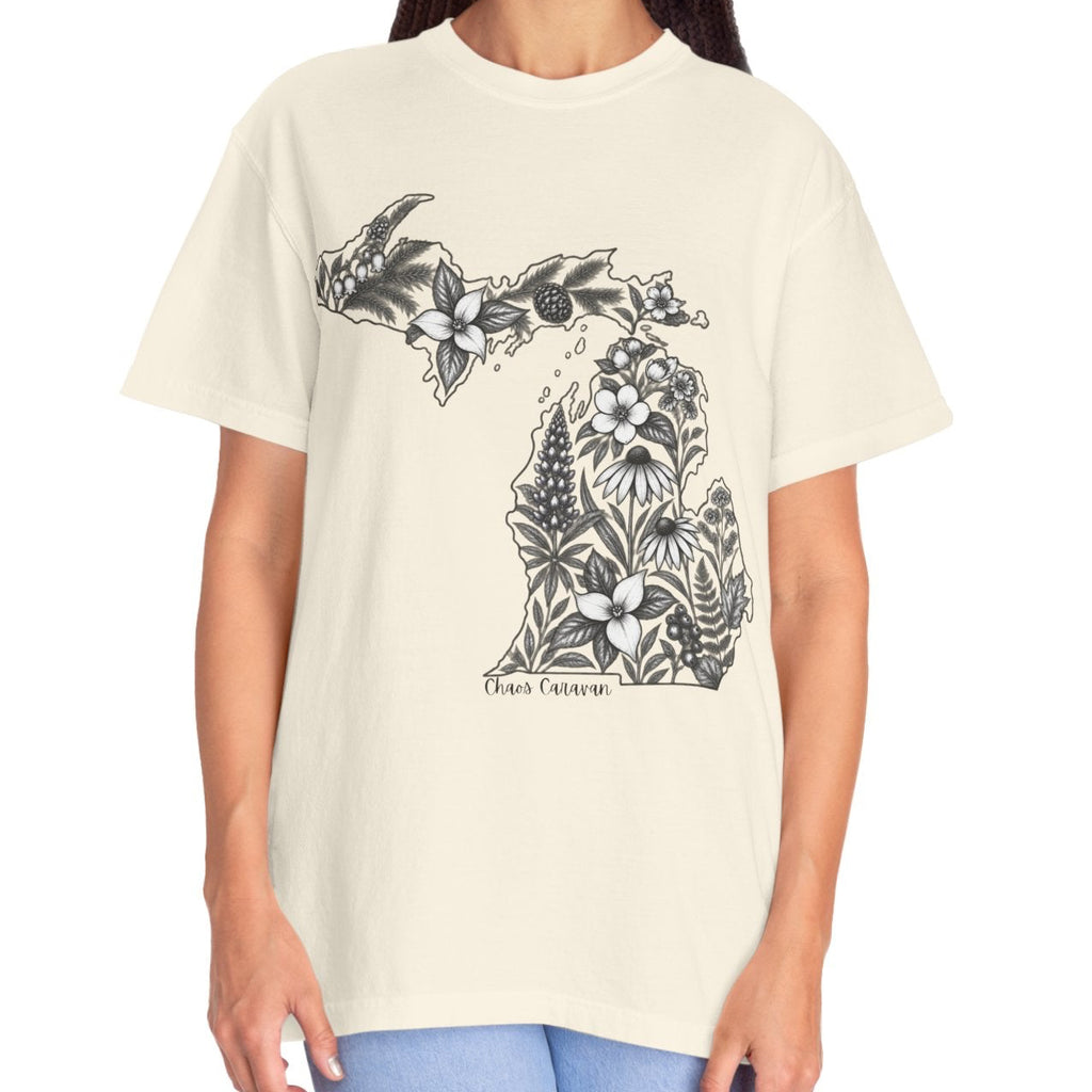 A woman modeling a cream-colored short-sleeve t-shirt with a black graphic of the state of Michigan filled with floral patterns, paired with light blue jeans against a plain white background.