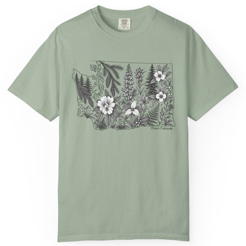 A sage green short-sleeve crewneck t-shirt featuring a black and white botanical illustration of the state of Washington filled with wildflowers on the chest, displayed against a clean white background.