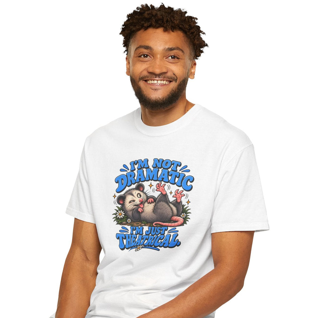 A man sitting on a black stool wearing a white graphic t-shirt and light blue jeans against a plain white background. The t-shirt features a colorful cartoon sloth graphic with the text 'I'M NOT DRAMATIC, I'M JUST THEATRICAL'.