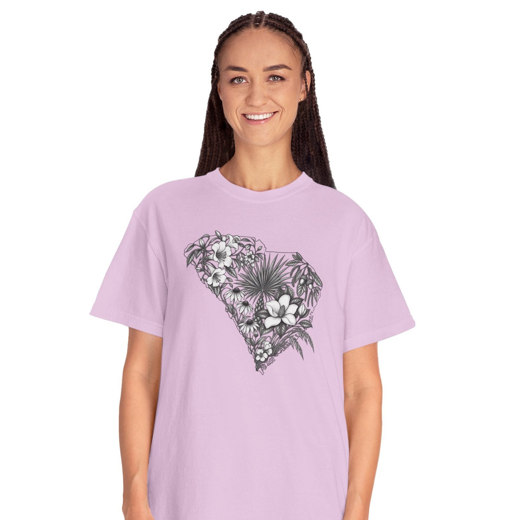 A woman modeling a light purple short-sleeve t-shirt with a black and white tropical floral graphic on the chest, paired with light blue jeans, against a plain white background.