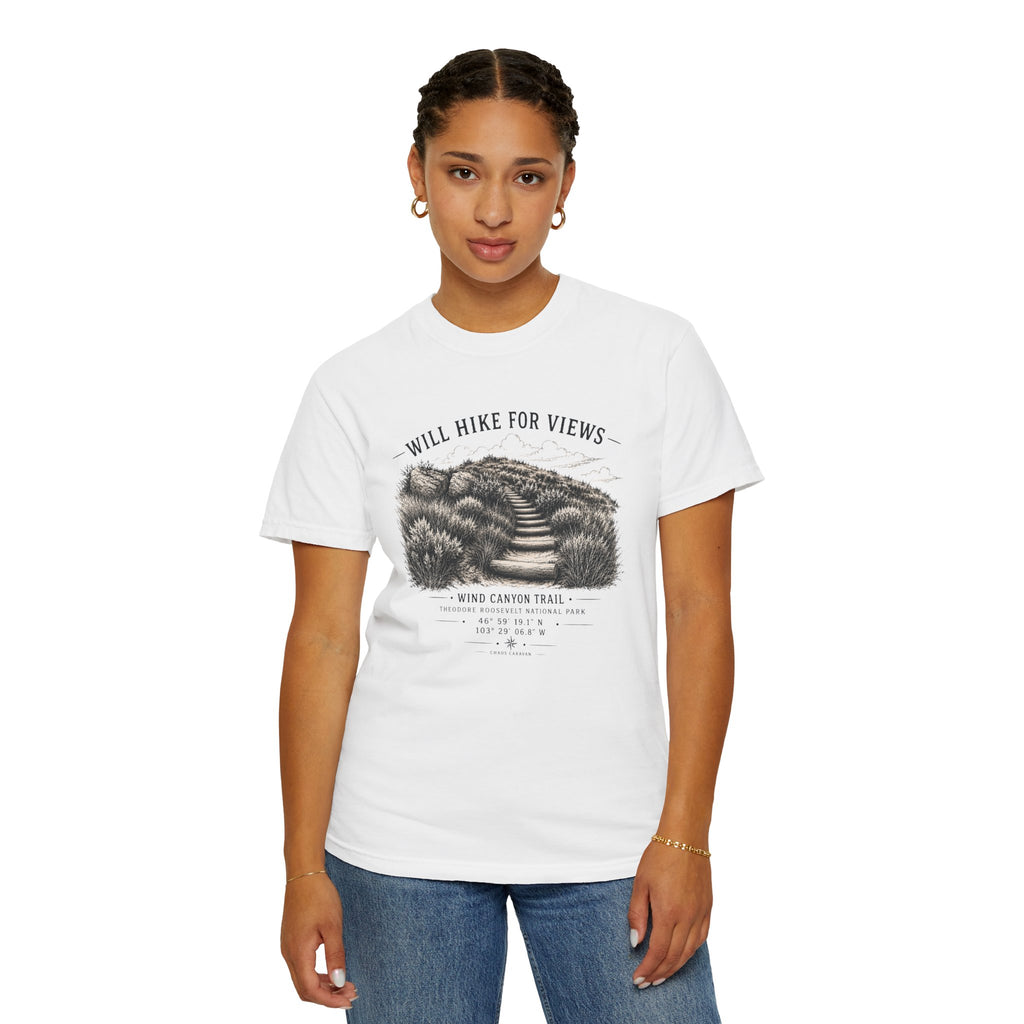 A woman modeling a white short-sleeve graphic t-shirt with a black and gray hiking illustration and the text 'WILL HIKE FOR VIEWS' and 'WIND CANYON TRAIL'. She is wearing blue jeans against a plain white background.
