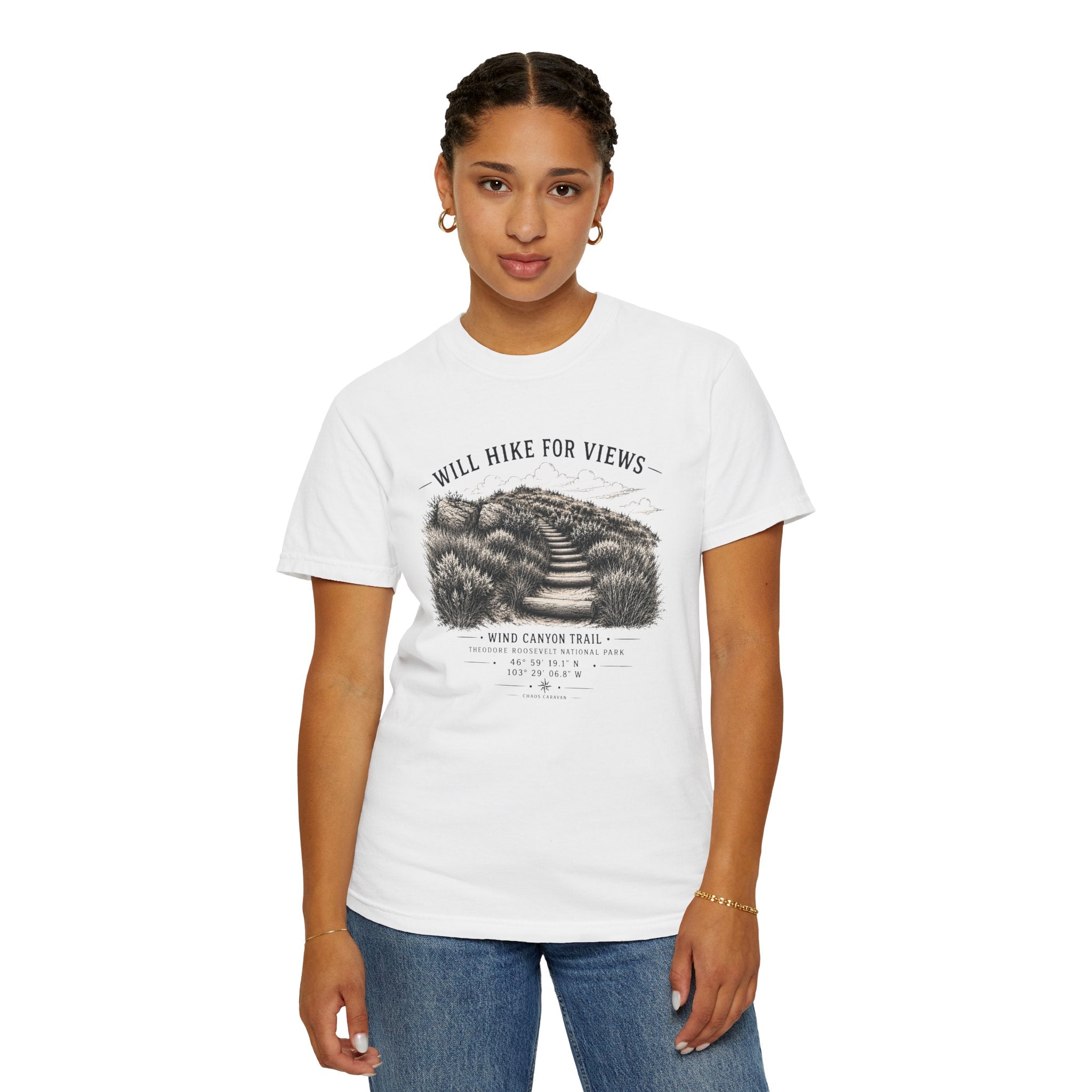 A woman modeling a white short-sleeve graphic t-shirt with a black and gray hiking illustration and the text 'WILL HIKE FOR VIEWS' and 'WIND CANYON TRAIL'. She is wearing blue jeans against a plain white background.