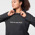 Person wearing a black hoodie with 'LINE UP AND WAIT.' text on a black background
