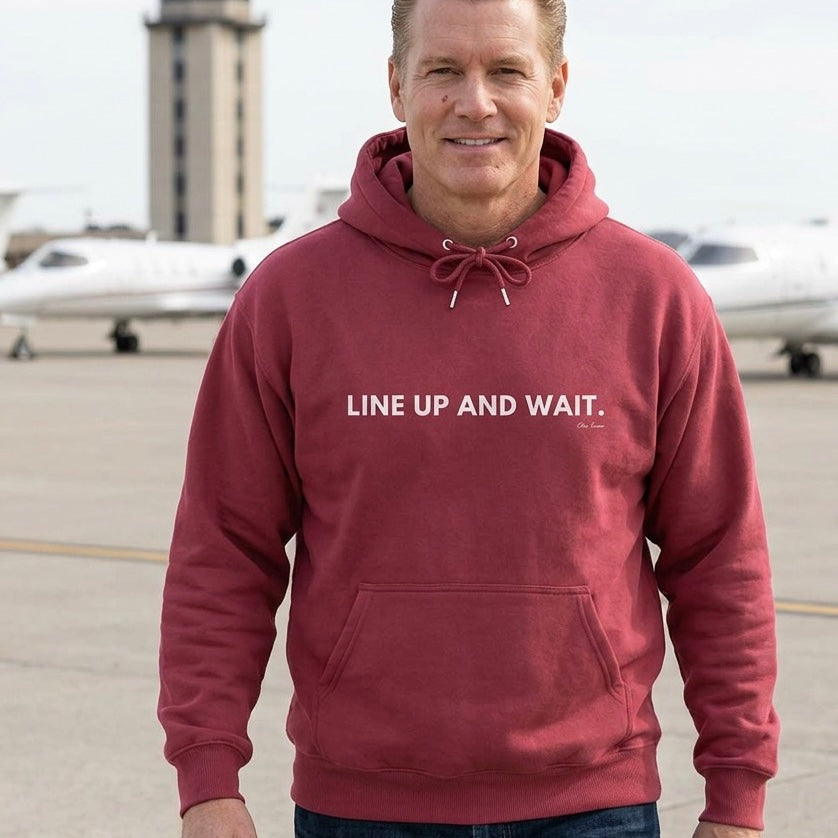 Man wearing a maroon hoodie with 'LINE UP AND WAIT' text on an airport tarmac.